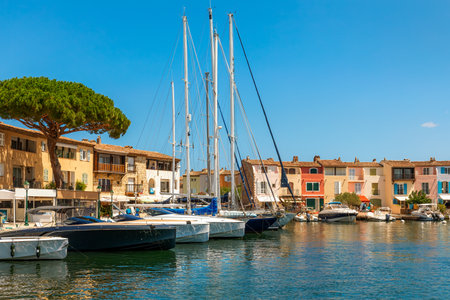 View of the harbor with several boats and yachts docked along the waterfront as colorful houses line the quay under clear blue sky in Port Grimaud, France.の写真素材