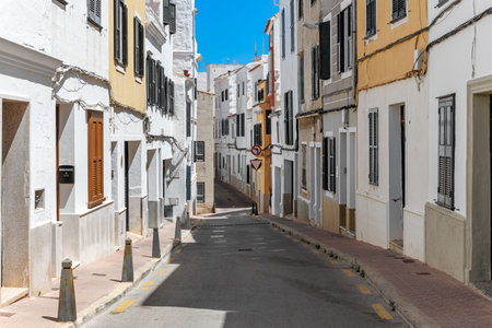 A quiet narrow street is flanked by traditional buildings with bright white walls in Mahon, Menorca, Spain.の写真素材