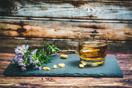 glass of whiskey on stone with rosemary flowers, lemon wedges and peanuts, wooden backgroundの写真素材
