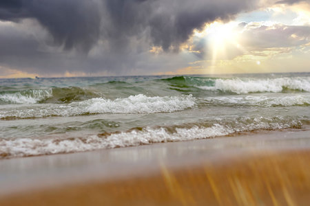 waves at sunset, which offer a beautiful landscape of this beach full of warm colors, with a cloudy sky and a calm beachの写真素材
