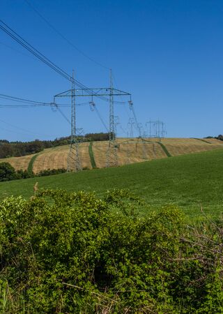 High-voltage power transmission towers over farm fieldsの写真素材
