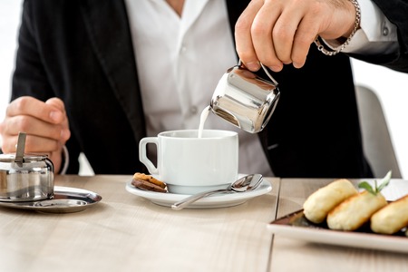 Businessman pouring milk to the cup of coffee at the restaurantの写真素材