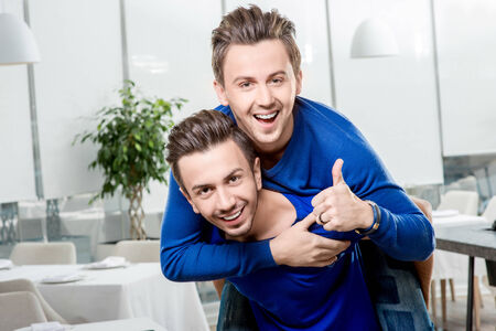 Friendly brothers twins having fun riding piggyback in the white home or restaurant interior. Family relationship between two brothersの写真素材