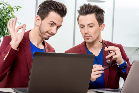 Two brothers twins in red jackets working with laptops and smart phones at the office. Family businessの写真素材