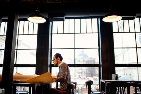 Creative architect projecting with pencil on the big drawings in the dark loft office or cafe. General plan with windowsの写真素材