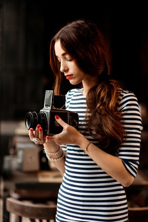 Young woman photographer with old 6x6 frame camera standing near the big window in the cafeの写真素材
