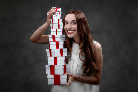 Young and excited woman with high hill of present boxes on her birthday or Valentines day in studioの写真素材