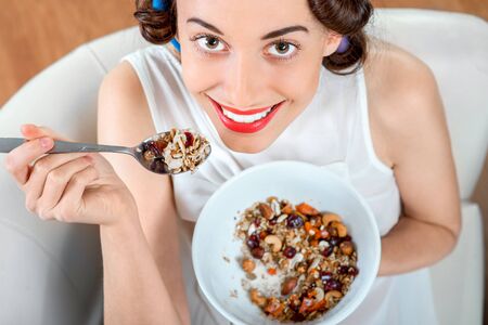 Young woman with hair curlers eating granola breakfast sitting on the couch at homeの写真素材