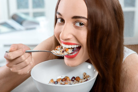 Young positive woman eating granola breakfast on the couch at home. Close-up