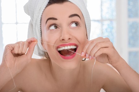Woman wrapped with white towel flossing teeth smiling, happy with perfect teeth and toothy smile in home bathroomの写真素材