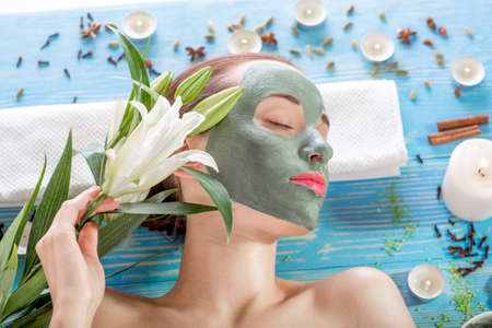 Young woman with spa facial mask on her face lying on blue table with flower, candles and sea salt in the beaty salonの写真素材