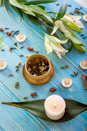 Cup of herbal tea on the wooden blue table with flower, candles, soap and herbals in spa salonの写真素材