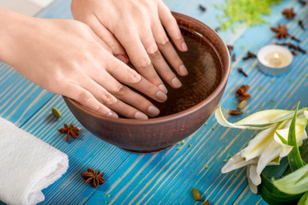 Soaking finger nails in the bath with water on wooden table with spa stuff on backgroundの写真素材