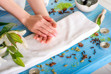Woman taking care of her hands on the bath towel in spa with flower, candles and herbs on blue wooden deskの写真素材