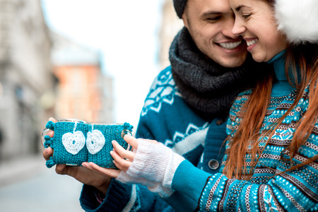Young loving couple dressed in blue sweater sitting with knitted coffee cups on the bench at the old city in winterの写真素材