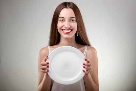 Young woman showing empty plate. Woman with plate in studio on white backgroundの写真素材