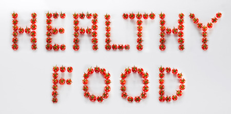 White board with tomatoes cherry on it set out the words HEALTHY FOOD isolated in studioの写真素材