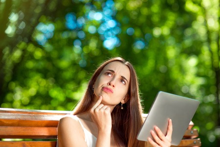 Young woman thinking with digital tablet on the bench at the parkの写真素材
