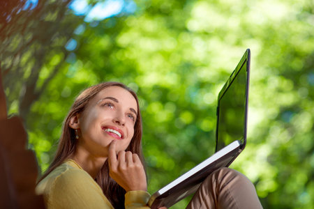 Young woman thinking, having idea wihle typing something in laptop at the parkの写真素材