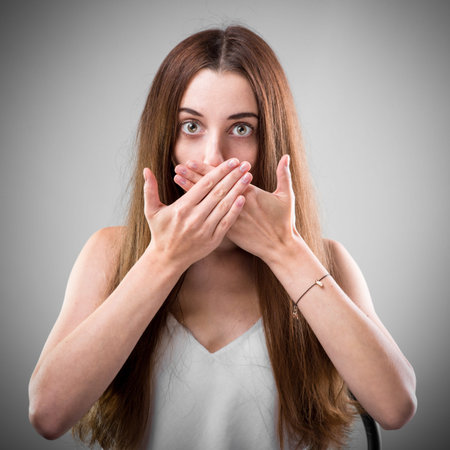 Studio portrait of young woman that don't want to speak on grey backgroundの写真素材