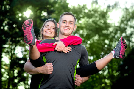 Happy sports couple in sportwear riding piggy back in the parkの写真素材
