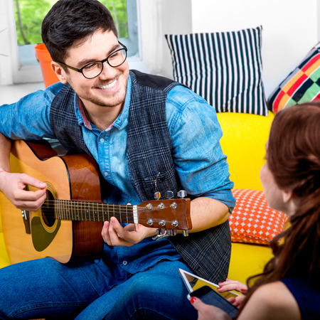 Handsome smiling man playing acoustic guitar on the yellow couch at homeの写真素材