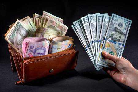 Pile of Ukrainian money in the wallet and american dollars in the hand on black background