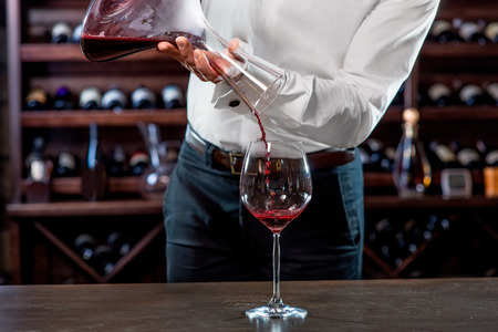 Sommelier pouring wine to the glass in the wine cellarの写真素材
