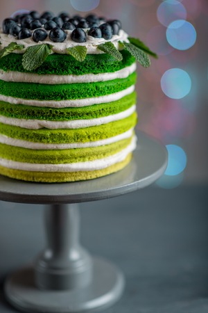 Nice sponge happy birthday cake with mascarpone and grapes on the cake stand on festive light bokehの写真素材