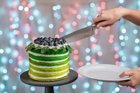 Cutting beautiful green sponge cake on festive background with bokeh lightの写真素材