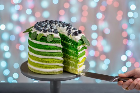 Cutting beautiful green sponge cake on festive background with bokeh lightの写真素材