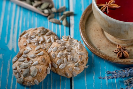 Sweet cookies with sunflower seeds and a cup of red tea with seasonings on blue wooden tableの写真素材