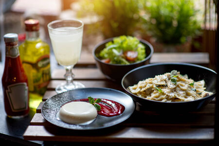 Italian dinner with pasta, panakota and salad on wooden table with blurred backgroundの写真素材