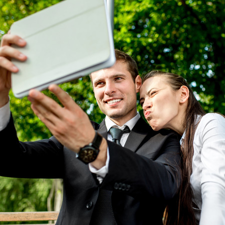 Young Business couple sitting on the bench and making selfie photo with tabletsの写真素材