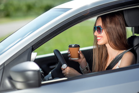 Young woman drinking coffee while driving her carの写真素材