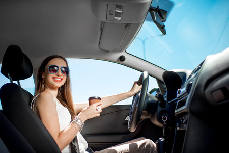 Happy young woman with coffee to go driving her car