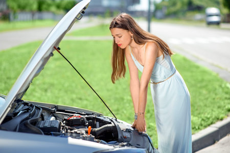 A woman waits for assistance near her car broken down on the road side.