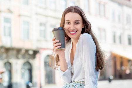 A businesswoman with cup of coffee to go against sunny city landscapeの写真素材