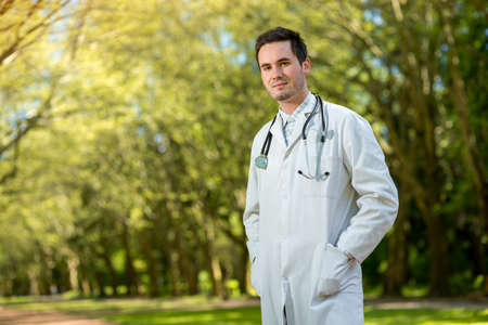 Young doctor portrait with stethoscope on the green park backgroundの写真素材