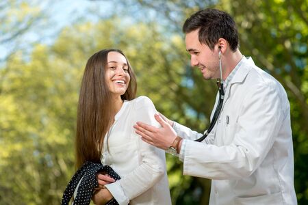 Young doctor listnening with stethoscope to the woman in the parkの写真素材