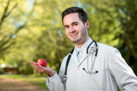 Smiling doctor keeping an apple in hand in the parkの写真素材