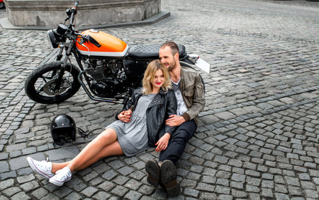 Couple lying on the paving and embracing near the motorcycle in the old city