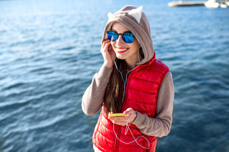 Young woman dressed in sportswear talking phone on the promenade near the water