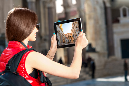 Young woman traveler photographing with tablet in the old city centerの写真素材