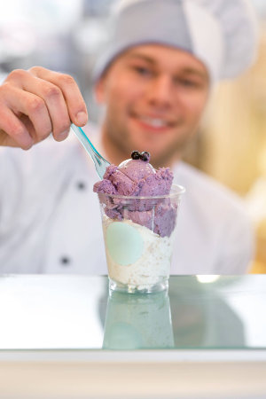 Handsome confectioner decorating ice cream with berry in the storeの写真素材