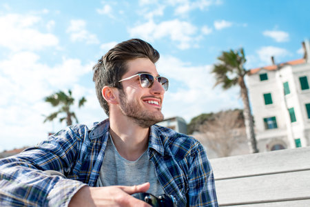 Professional photographer in casual clothes holding camera on the bench in the tropical cityの写真素材