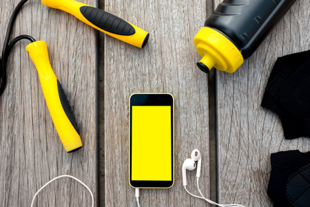 Mobile phone with empty screen on the wooden desk surrounded with sport equipment. Sport mobile...