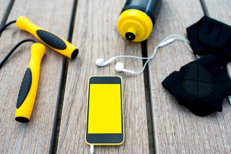 Mobile phone with empty screen on the wooden desk surrounded with sport equipment. Sport mobile application conceptの写真素材