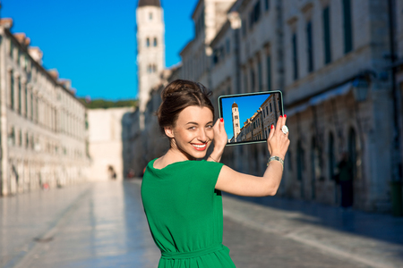 Young woman photographing with digital gadget bell tower in Dubrovnik old city centerの写真素材