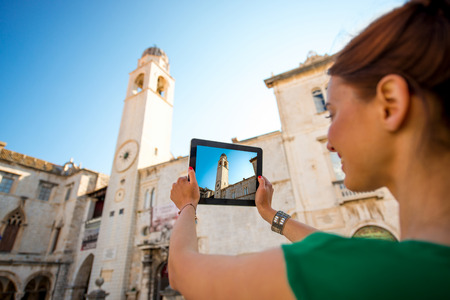 Young woman traveler photographing clock tower with digital tablet in Dubrovnik old city center.の写真素材